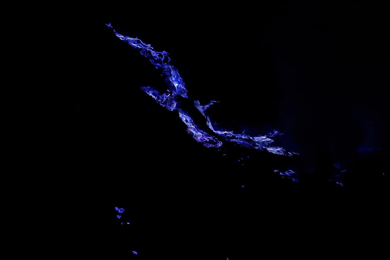 Electric-blue flames rising from sulfur vents at Kawah Ijen in the dark, East Java, Indonesia.
