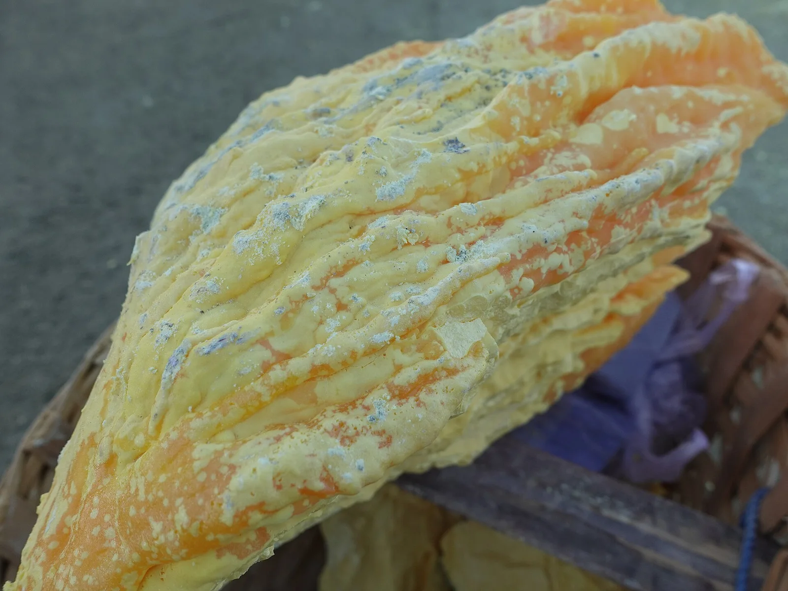 A large chunk of solidified yellow sulfur resting in a miner's woven basket at Kawah Ijen.